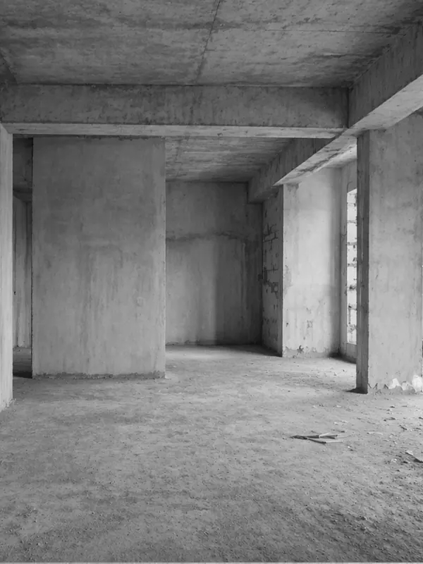 Raw unfinished interior with exposed concrete walls, structural columns, and an open floor plan under construction.