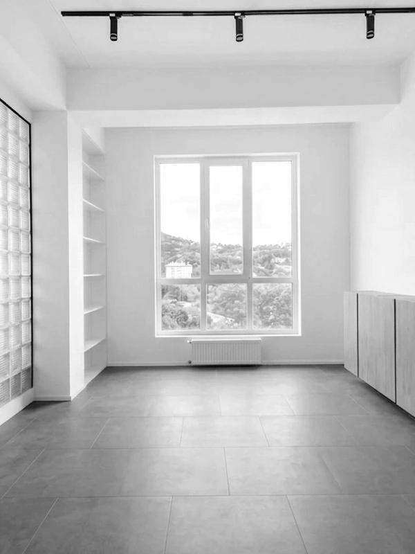 Minimalist empty room with gray floor tiles, a large window, built-in shelving, and track lighting