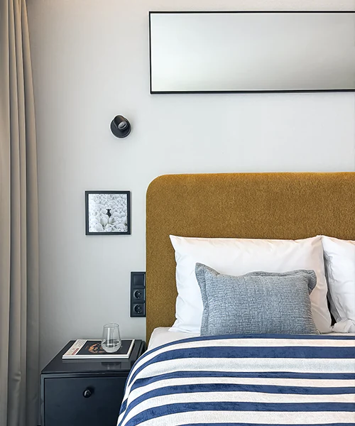Modern bed area with upholstered headboard, bedside cabinet, wall art and striped throw