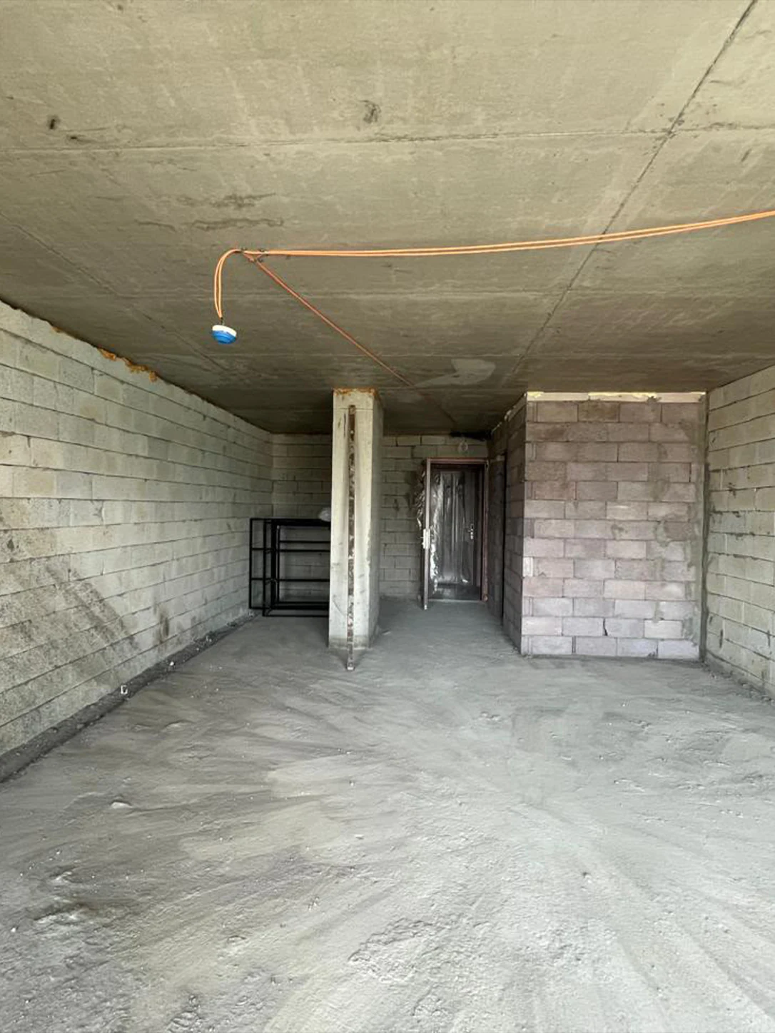 Unfinished apartment interior with exposed blockwork, a concrete column and the entrance door